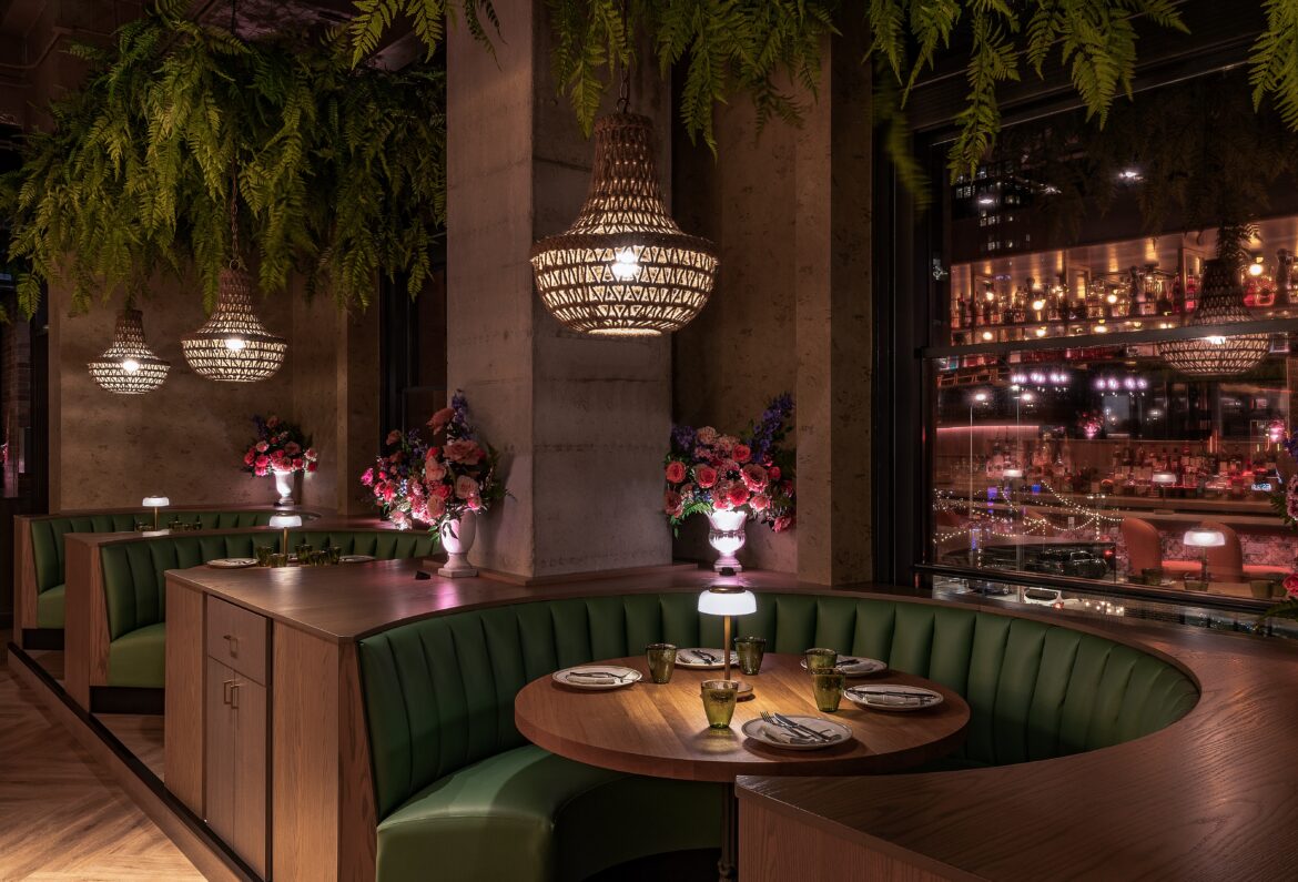 An upscale French restaurant with plants hanging from the ceiling and vases with pink and purple flowers along plush green booth seating