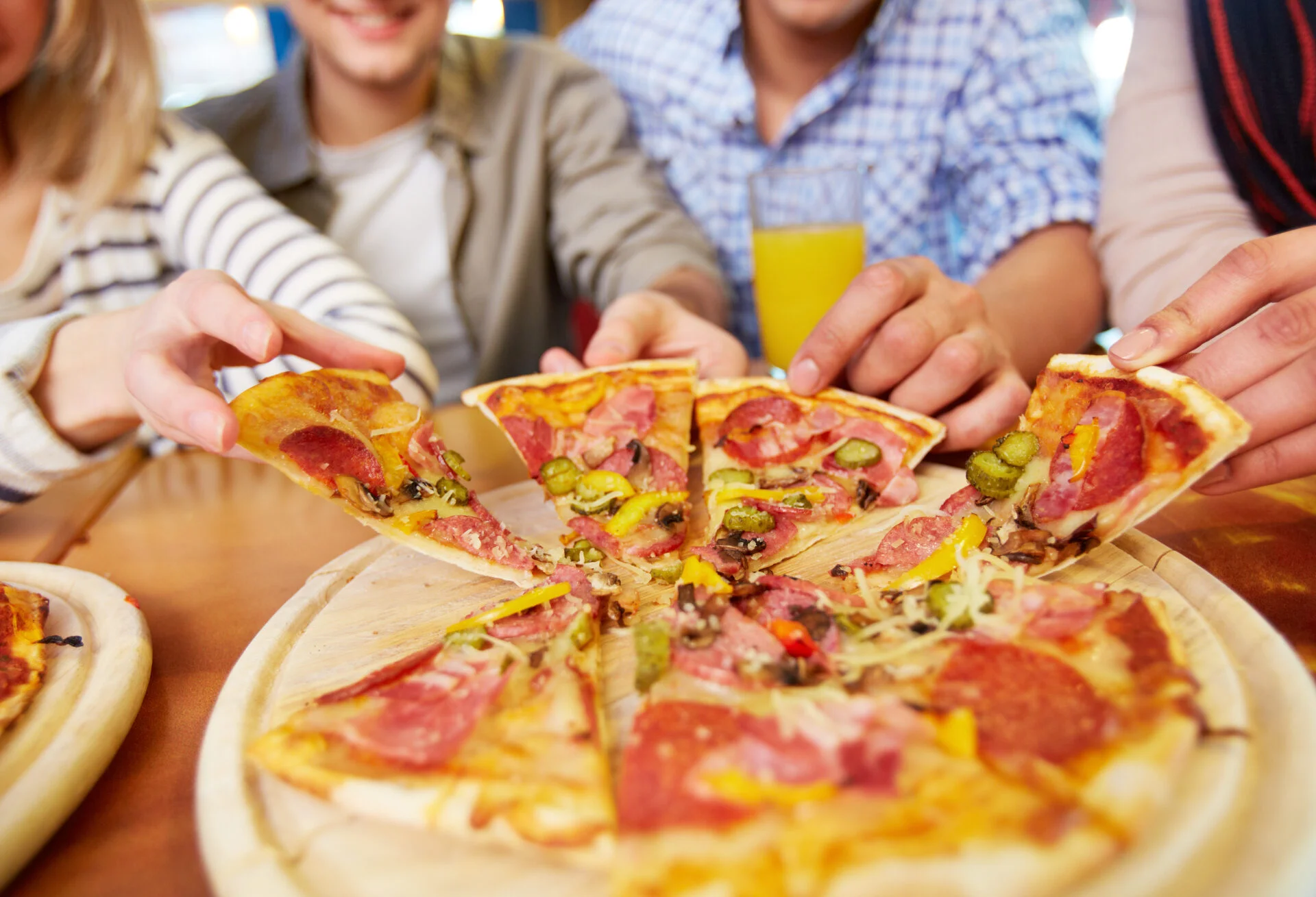 Image of teenage friends hands taking slices of pizza