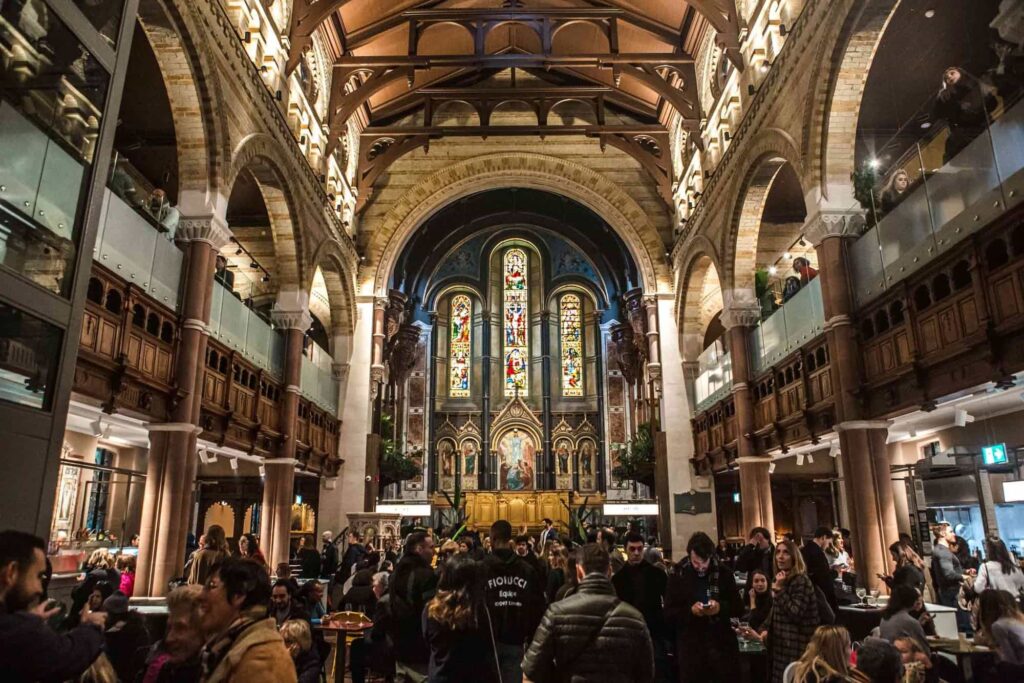 people milling about the main interior space at mercato mayfair with the impressive stained glass windows in the background