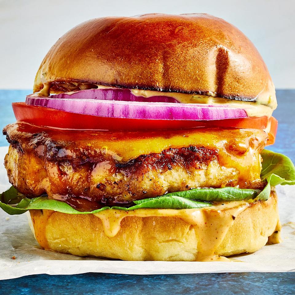 chicken burger topped with sauce, lettuce, sliced red onion, and tomato