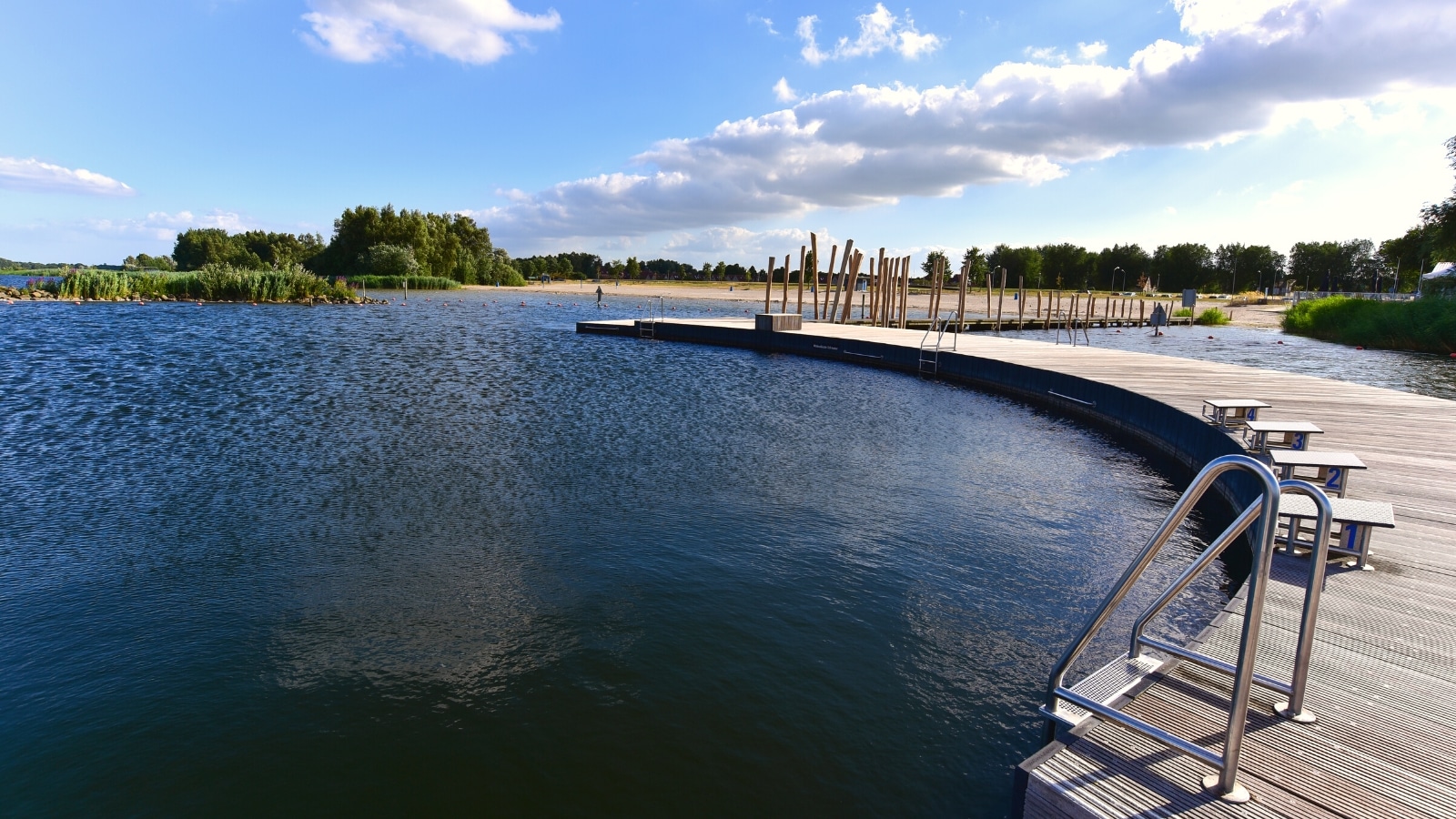 A straightforward photograph capturing a view of a lake with a pier, featuring greenery in the background.