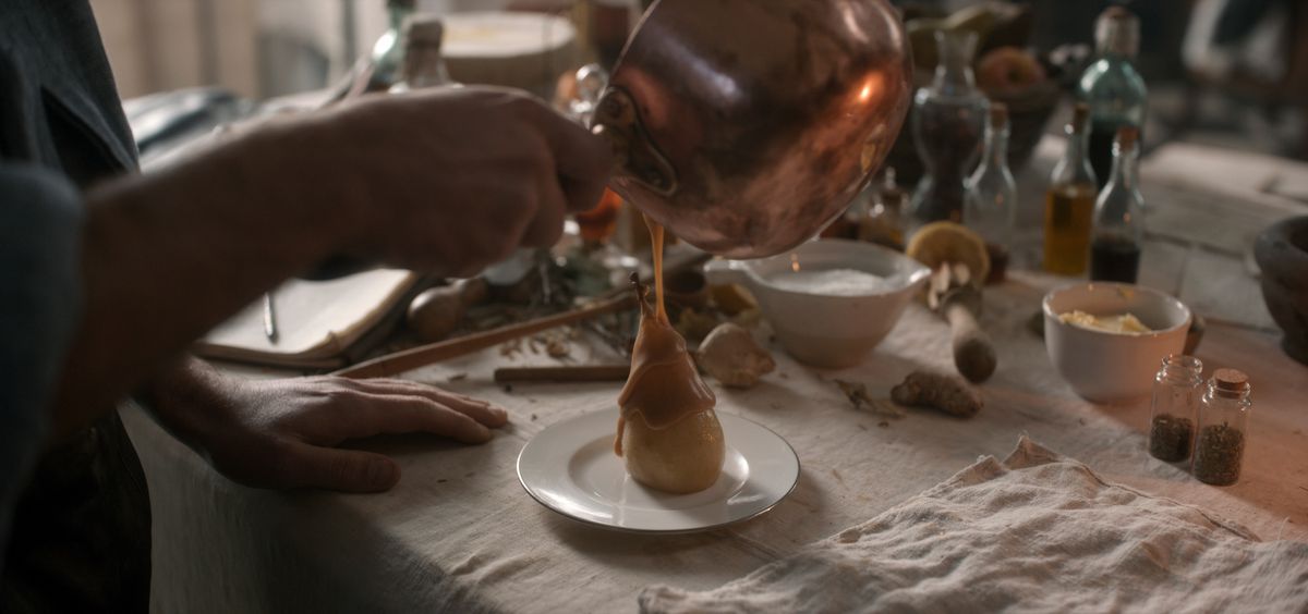 Hands pour caramel over a pear sitting upright on a white plate.