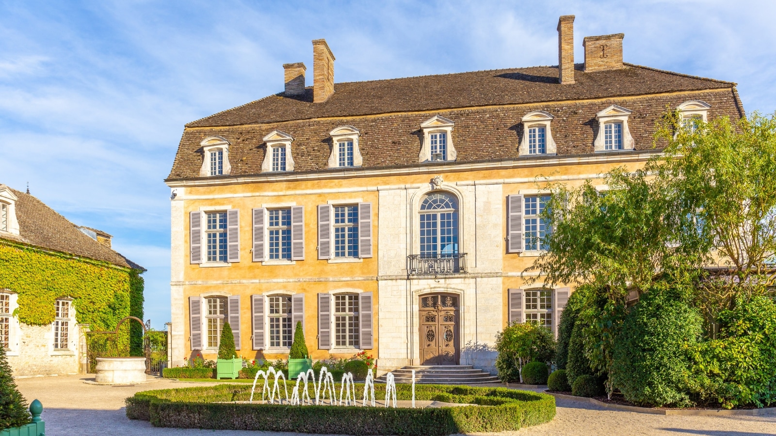 A photograph capturing Chateau de Pommard in Beaune, France. The image displays the exterior of the chateau, showcasing its architectural features. Surrounded by greenery, the chateau presents a serene atmosphere.