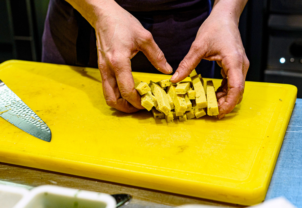 A chef gathers raw sticks of panisse on a cutting board.