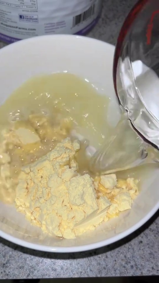 Water being poured into a bowl of yellow powder and liquid.