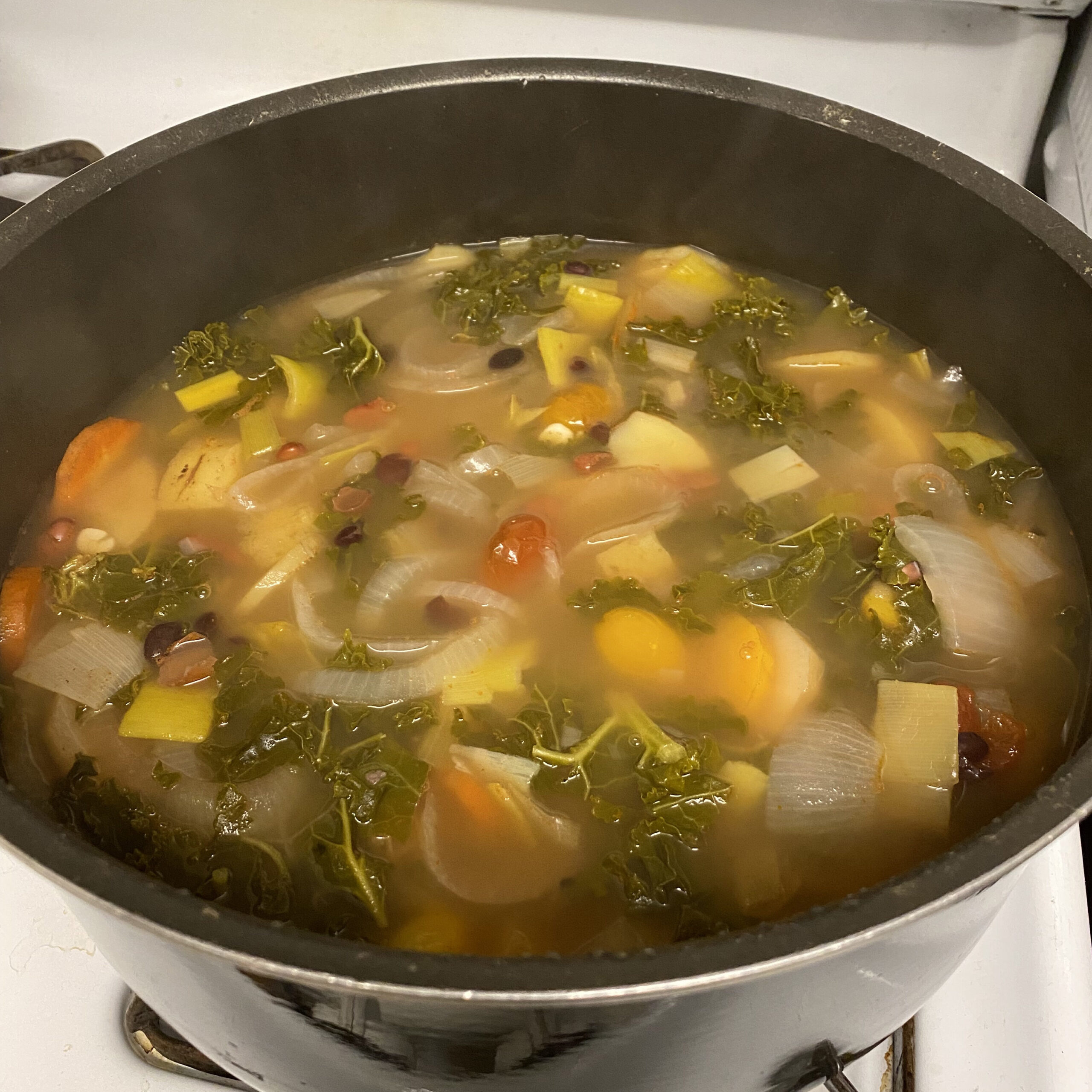 A pot of soup with onions, carrots, kale, and more in it.