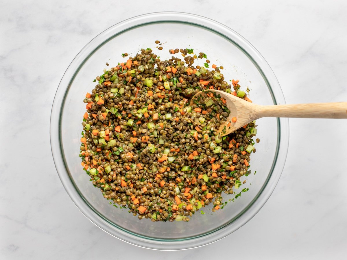 lentil salad mixed in bowl with wooden spoon.