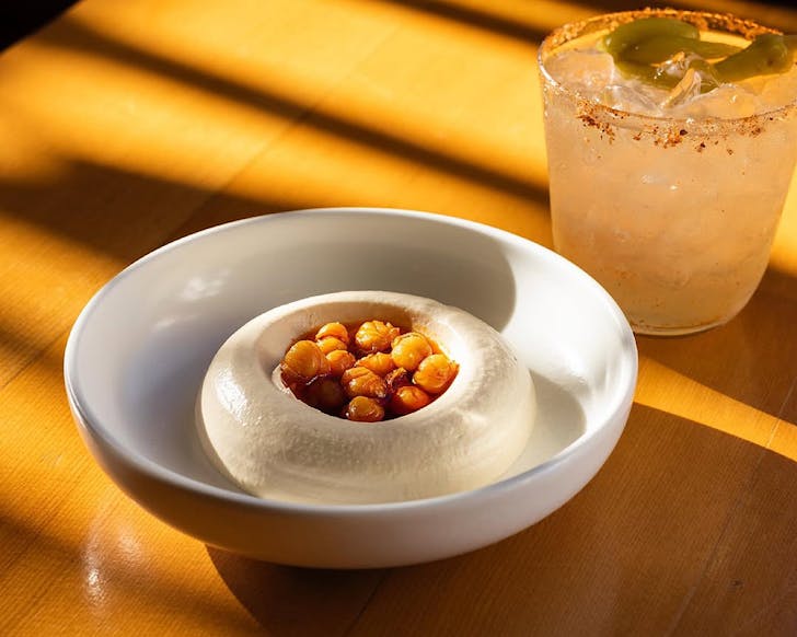 A bowl of hummus with chickpeas in the centre, and a spicy marg. 