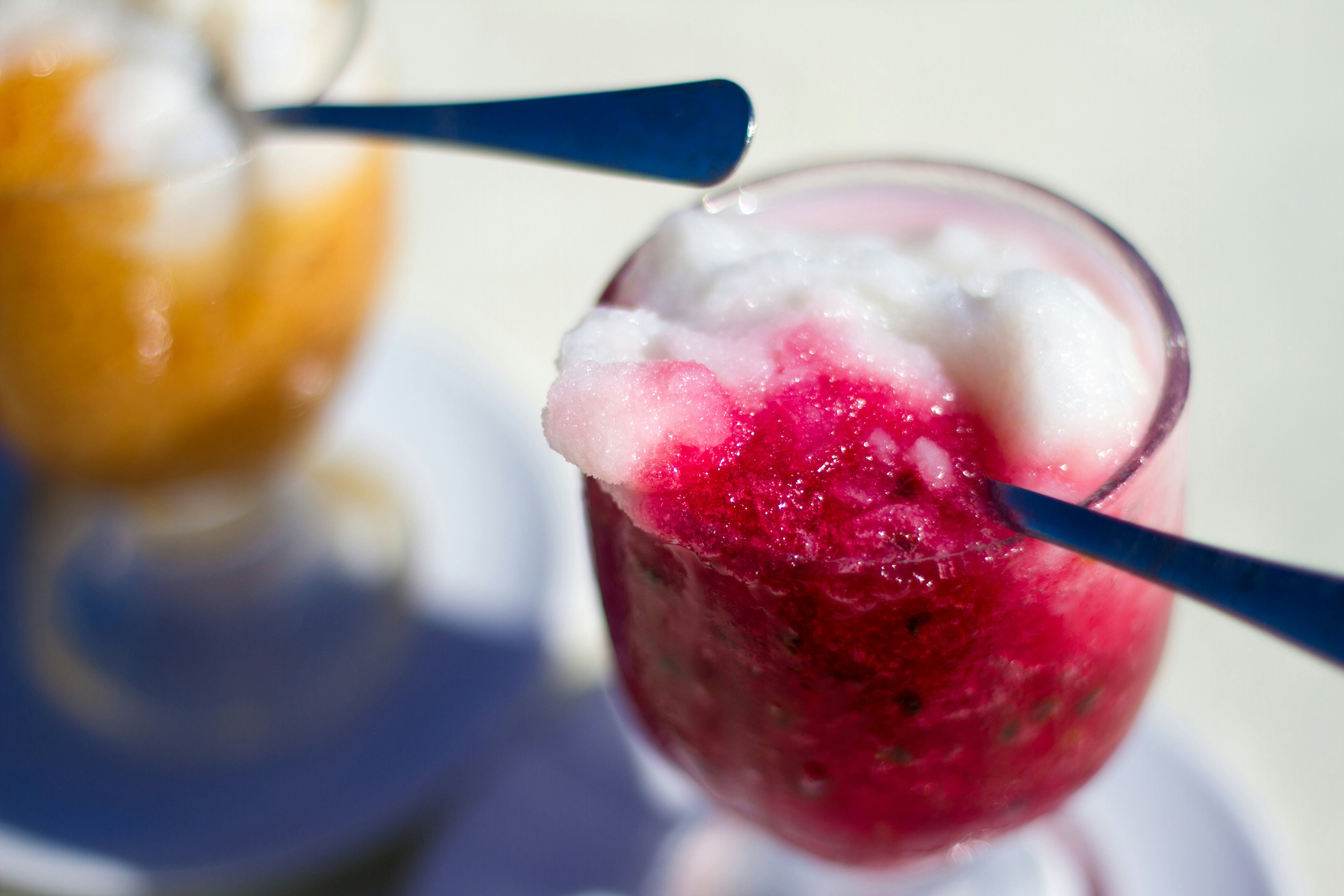 A spoon scooping out bright pink flavored ice from a glass.