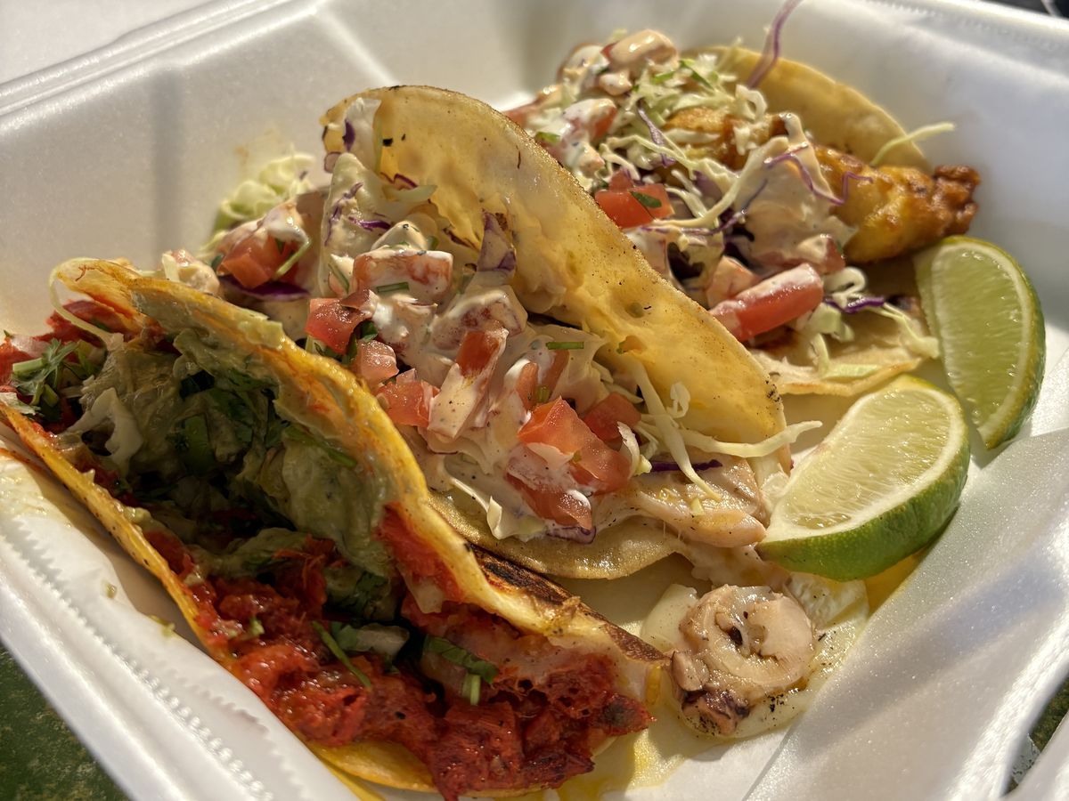 A trio of tacos with fish, octopus, and tuna, with lime wedges.