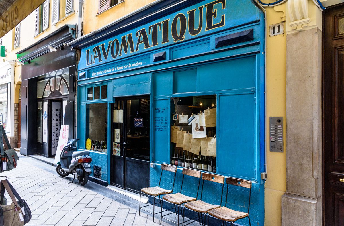 A bright blue restaurant exterior with charis places on the sidwalk outside.