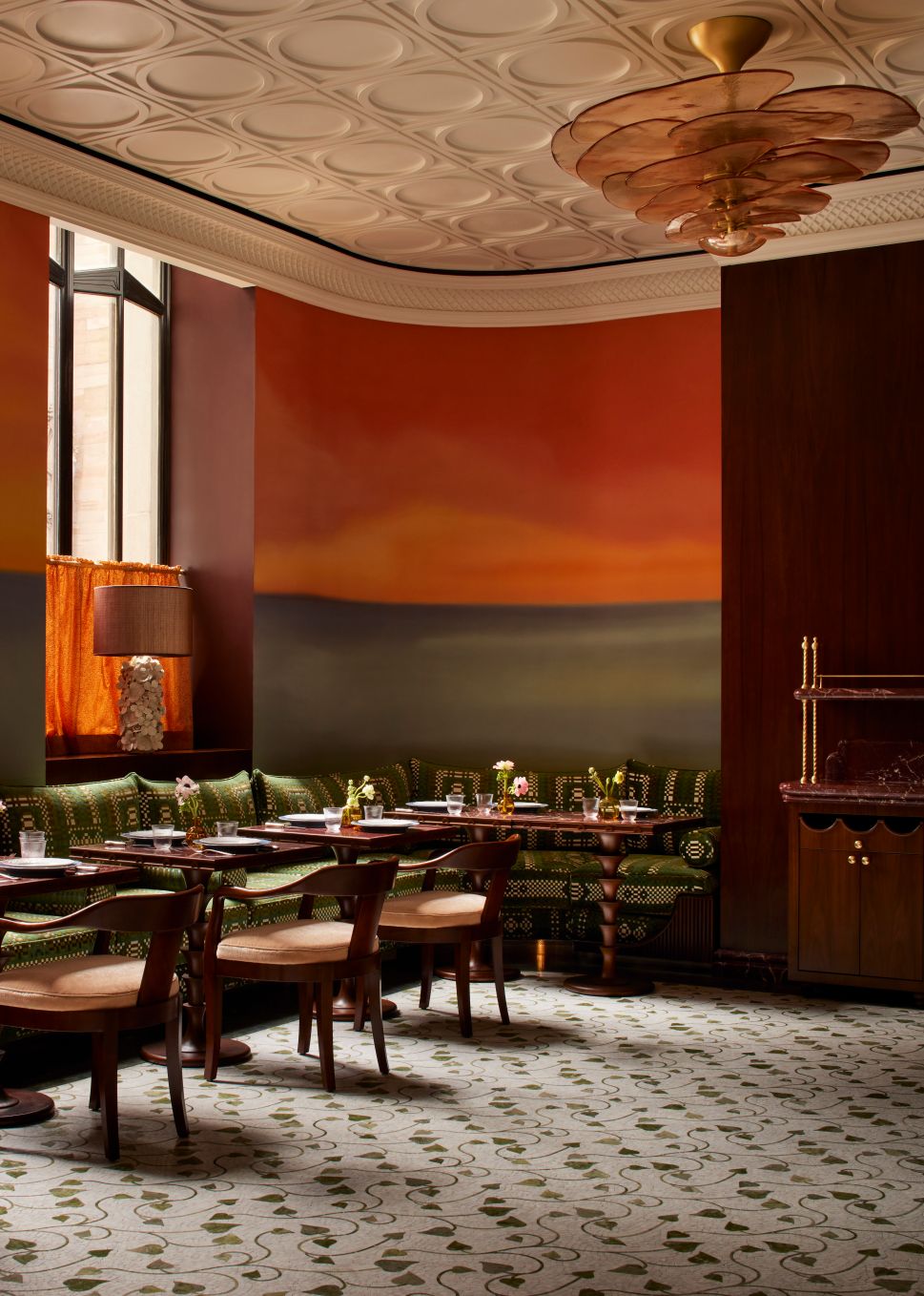 The dining room at Maison Passerelle features green patterned banquettes, midcentury chairs, and a sunset-hued wall mural.