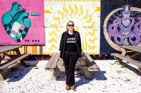 Restauranteur Marilyn Schlossbach stands in front of a colorful mural