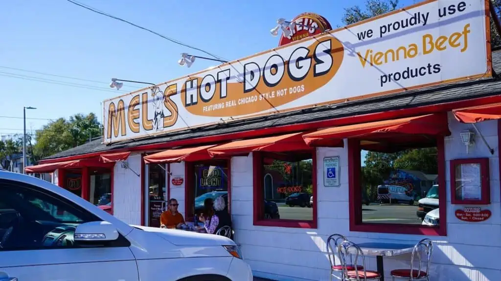 exterior of a restaurant with a large hot dog sign on the front. It's painted white, orange, red and yellow.