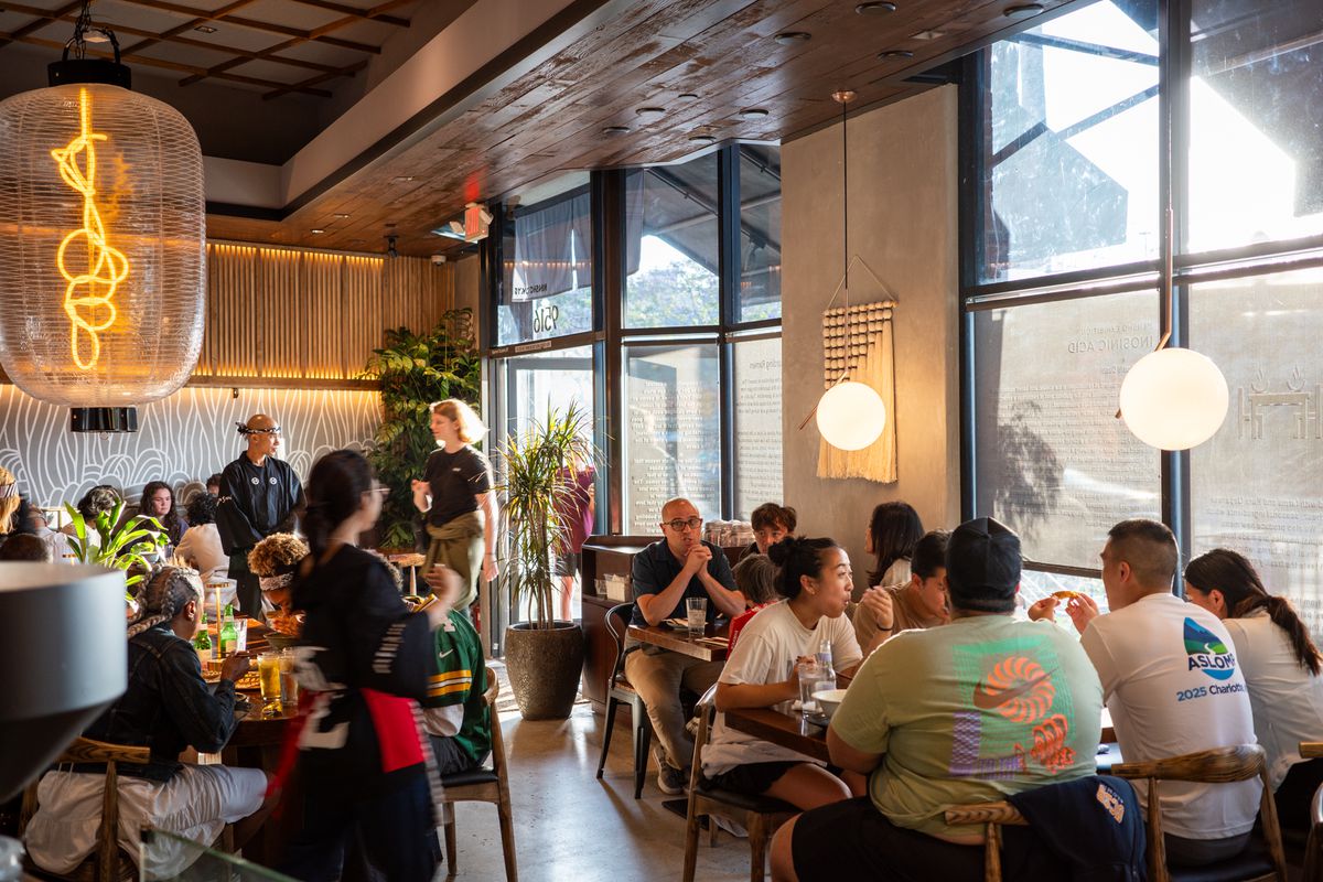 Patrons at a ramen restaurant with glowing hanging lamps.
