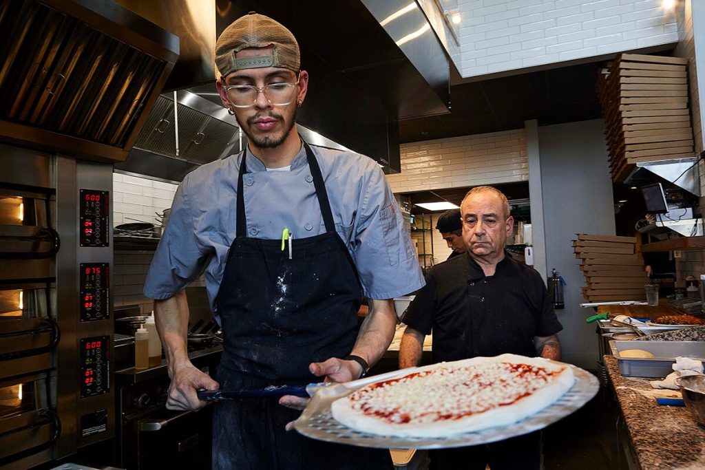 Richard Weiner (right), co-owner of No Regrets Pizza Co., keeps an eye on a pie as it goes into the oven.