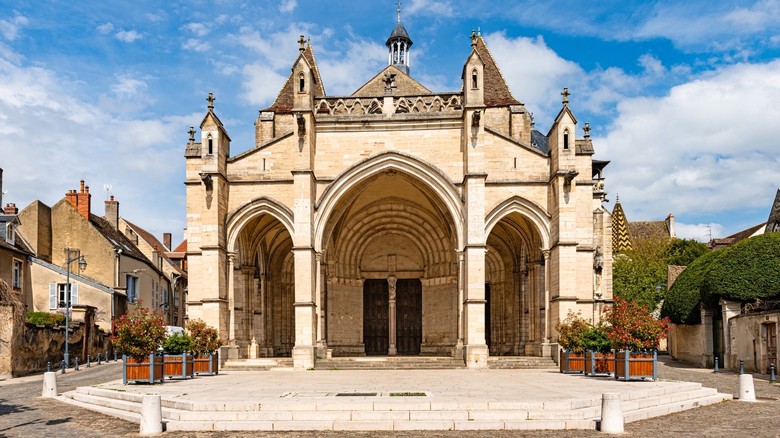 A photograph capturing the exterior of Notre Dame de Beaune. The image showcases the architectural features of the church, with its classic Gothic design and intricate details. The church is situated against a clear sky, allowing for a straightforward view of its facade and surroundings. 