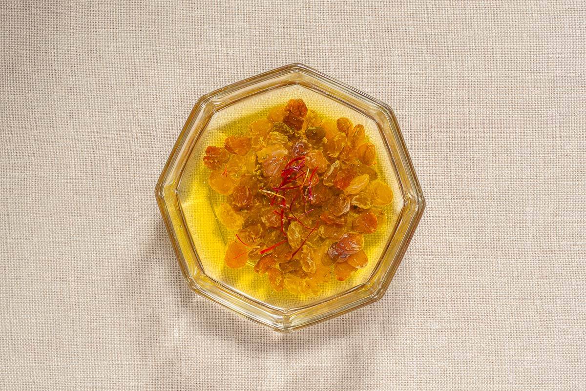 The raisins and saffron for the sardine pasta steeping in warm white wine in a bowl.