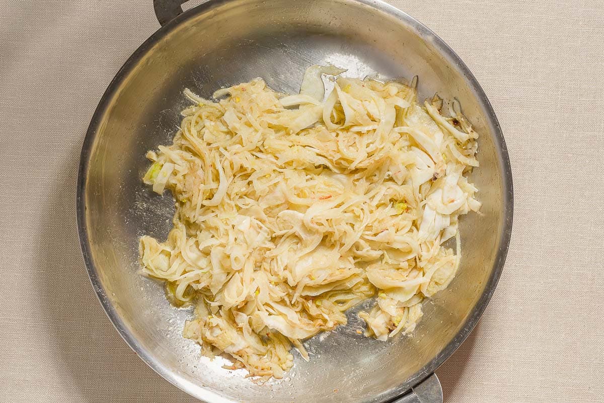 Sautéed sliced onions and fennel for the sardine pasta in a skillet.