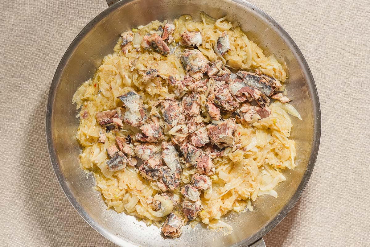Sautéed sliced onions, fennel, sardines and anchovy fillets for the sardine pasta in a skillet.