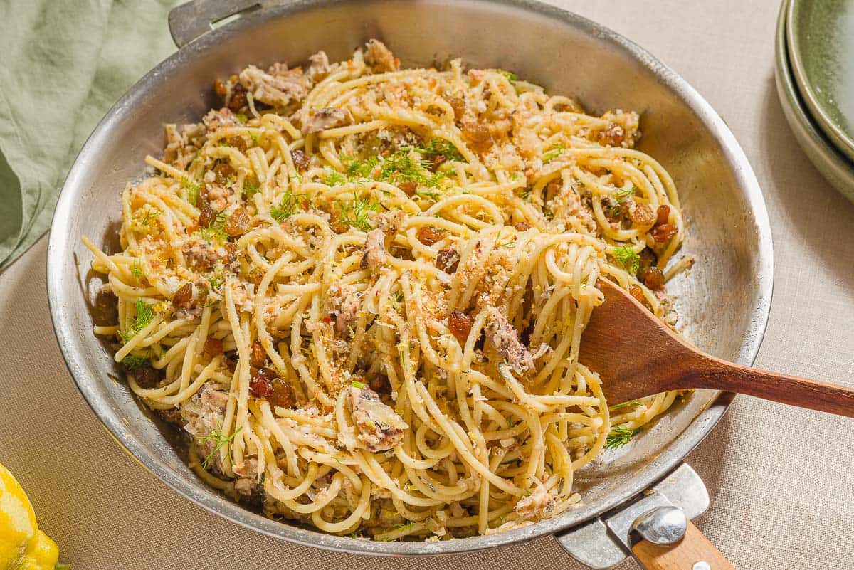 The sardine pasta in a skillet with a wooden spoon.