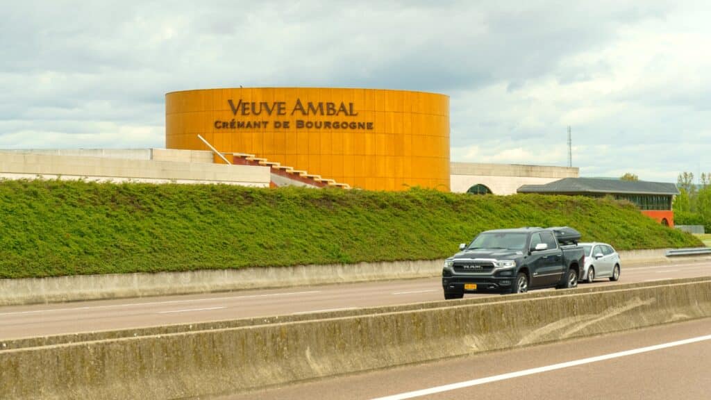 The image depicts a cone-shaped orange building with the inscription 'Veuve Ambal.' In the foreground, a road is visible with a car in motion. The building's distinctive color and shape, along with the prominent signage, make it a notable landmark