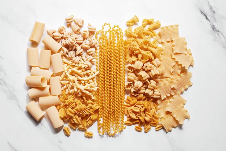 Photo of pasta in many different shapes on a marble countertop.