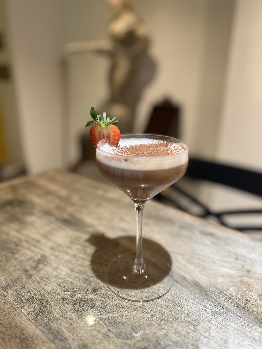 A pale brown, foam-topped espresso martini is garnished with a strawberry.