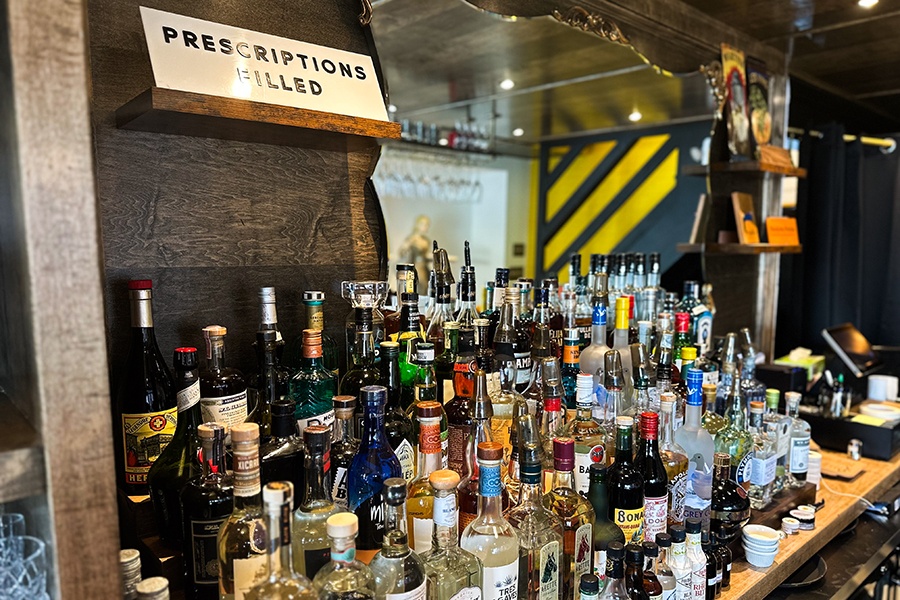 Shelves of liquor bottles on a backbar, decorated with signage that says 