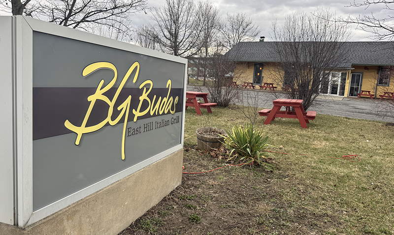 A sign in front of a low building says BG Budas east hill Italian grill