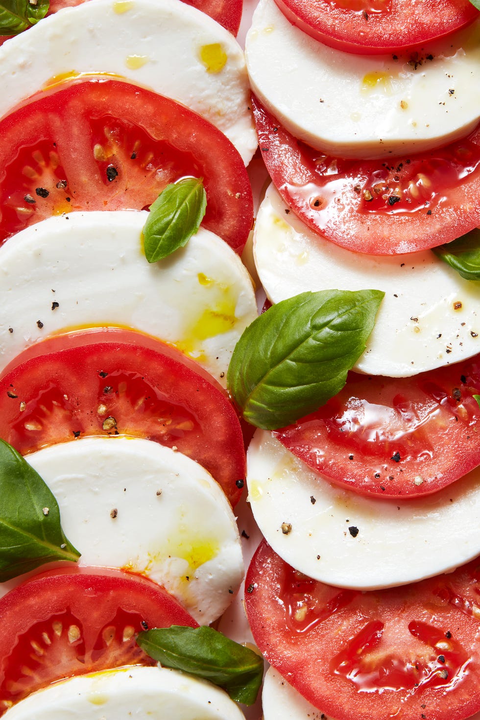 sliced tomatoes, mozzarella, and basil on a plate drizzled with olive oil