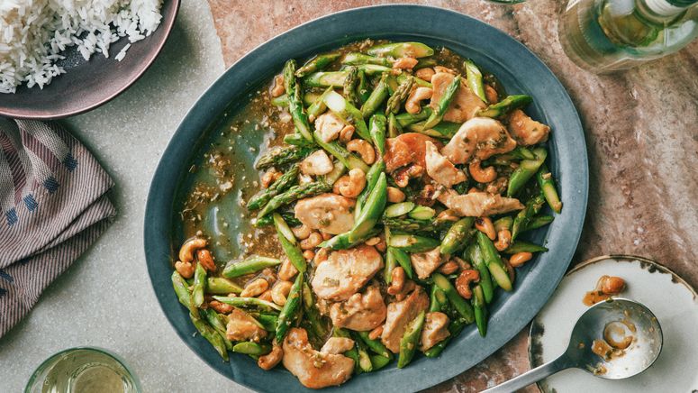 Chicken breast chopped asparagus and cashews in a sauce on a serving platter and served with rice.
