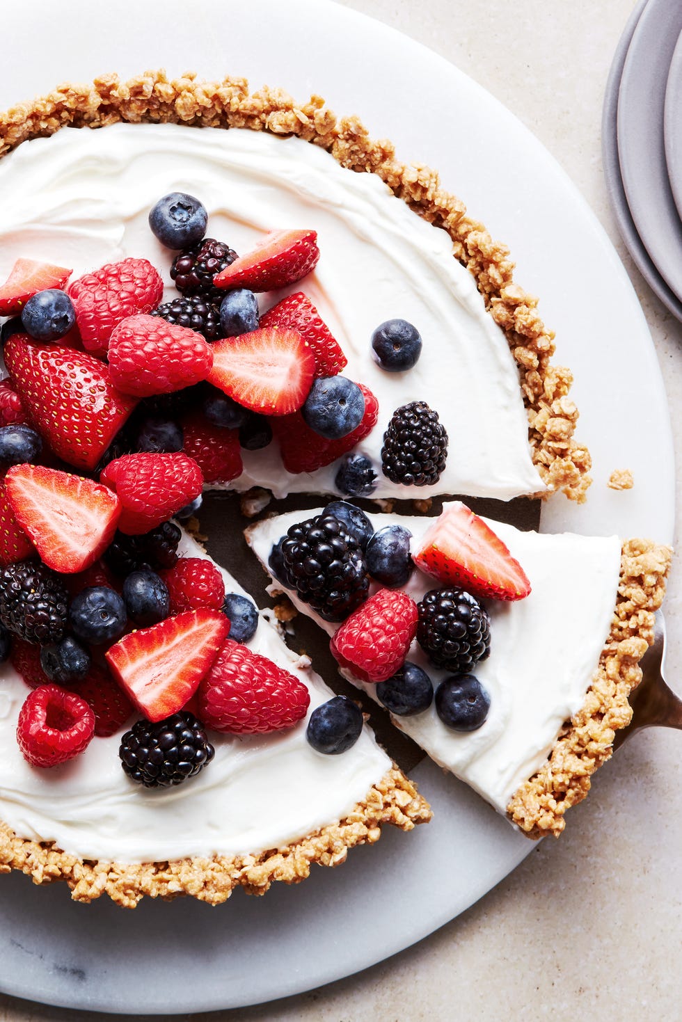 a slice of no bake fruit and granola breakfast tart coming out of the larger tart, topped with blueberries, blackberries, raspberries, and strawberries