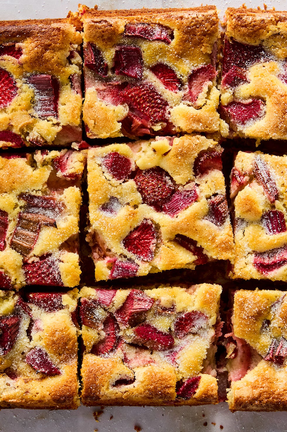 a tray of square slices of cake with strawberry and rhubarb pieces distributed throughout
