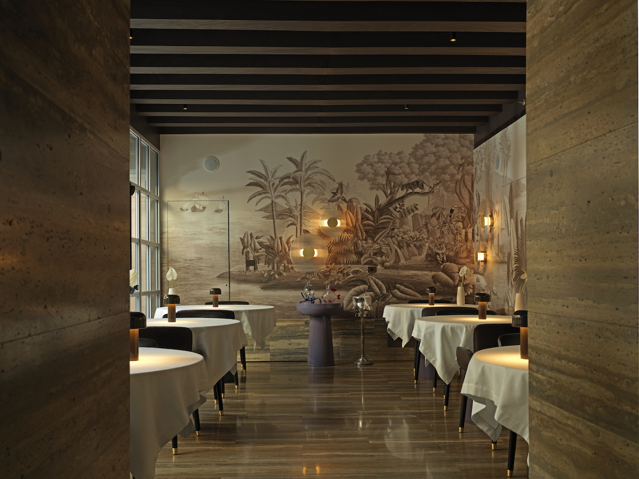 A dimly lit restaurant with nature-inspired murals, round-shaped, softly glowing lighting, round tables, mushroom table lamps, and sleek floors.