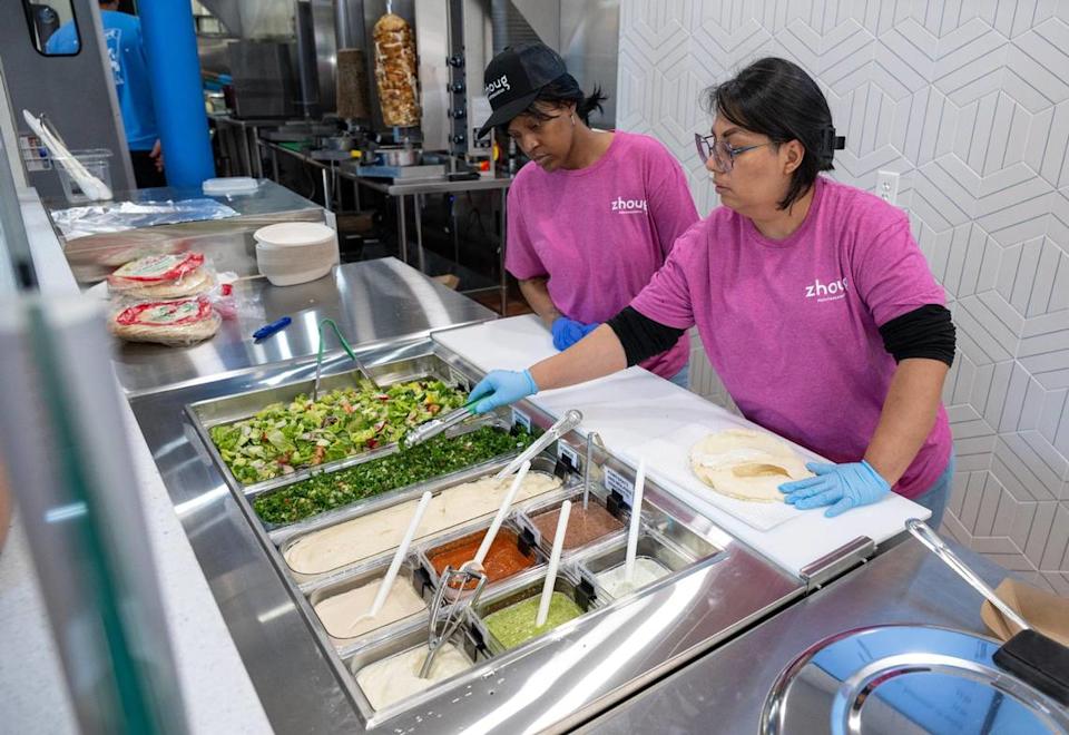 LaShaye Brooks, left, looks on as Karla Vazquez, right, makes a wrap during a soft opening at Zhoug Mediterranean’s new location.