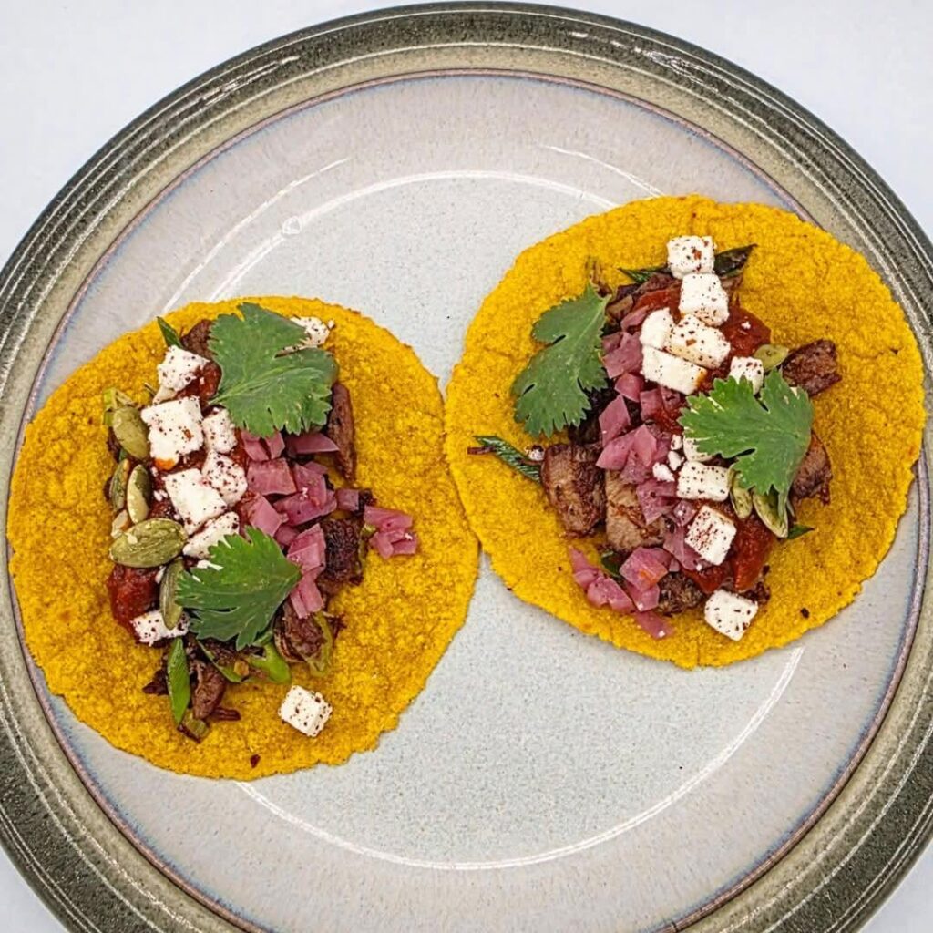 Lamb Vindaloo tacos with freshly made turmeric tortillas, 14 hour roasted lamb shoulder, extra spicy vindaloo sauce, sautéed green onions, paneer cheese, pickled purple onions, toasted pumpkin seeds, and fresh cilantro