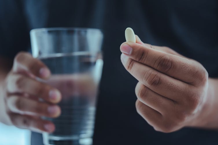 Man holding glass of water in one hand, white pill in other