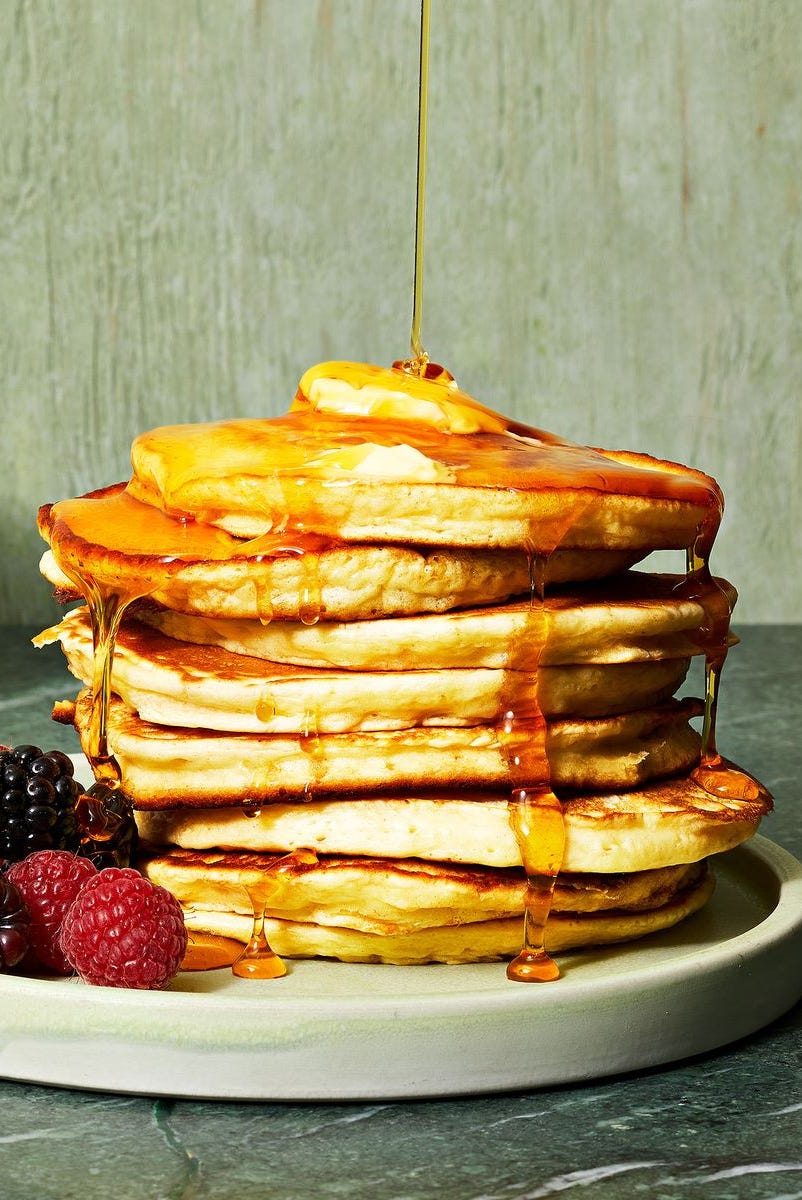 Fluffy Pancakes a stack of fluffy pancakes with syrup drizzled on top and a side of berries