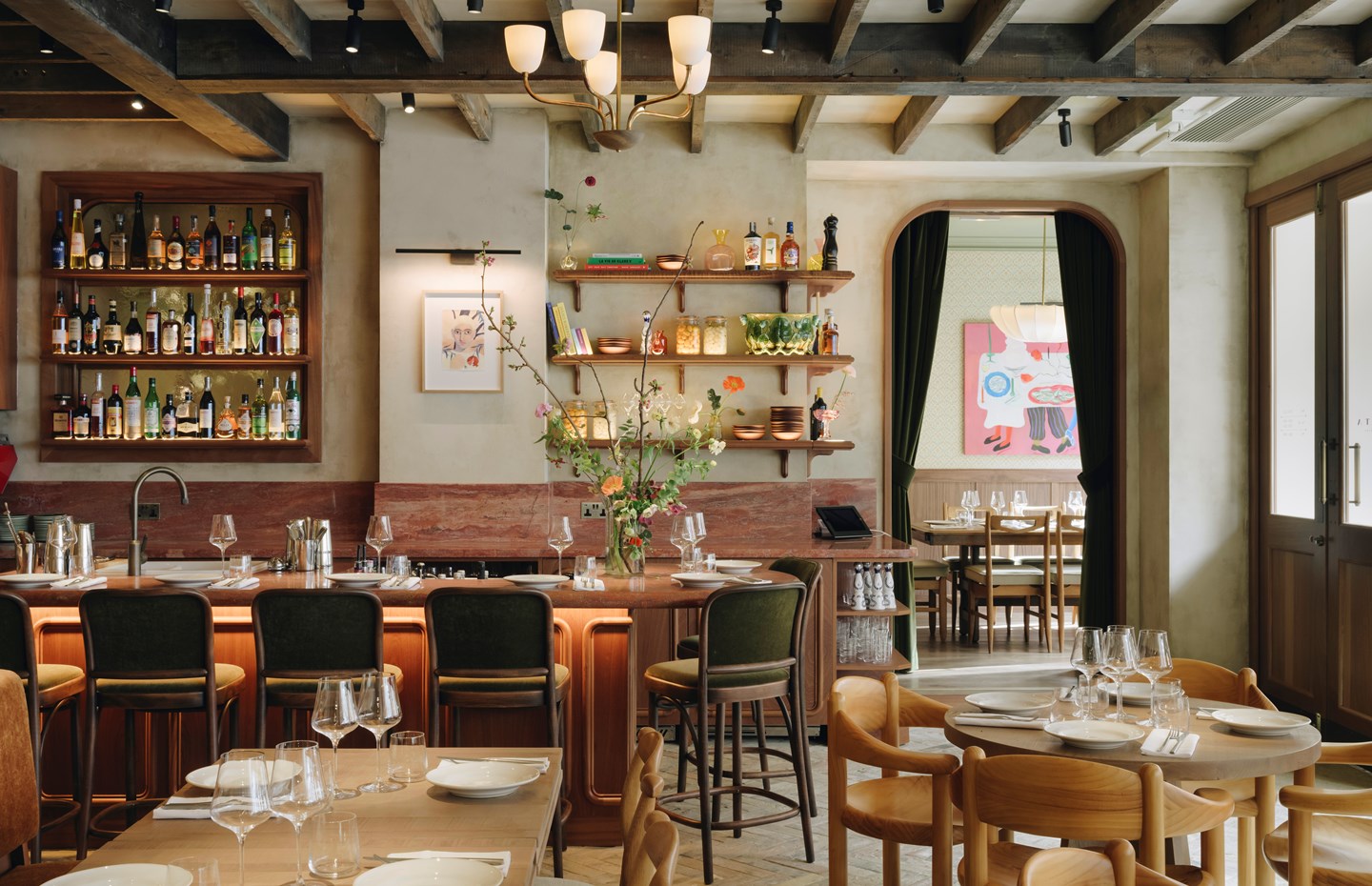 An earthy modern bistro with wooden surfaces and lavish green velvet accents is decorated with fantastical artworks, trailing flowers, and quirky collectibles.