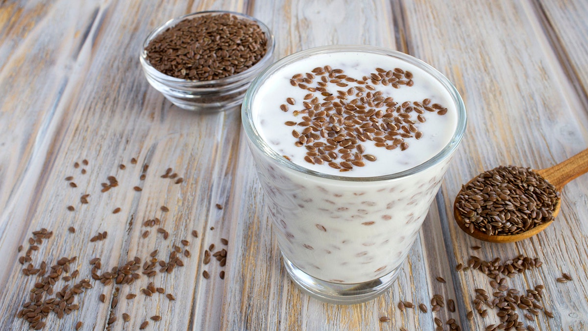 Yogurt or kefir with flax seeds in the drinking glass on the light brown wooden background. Close-up.