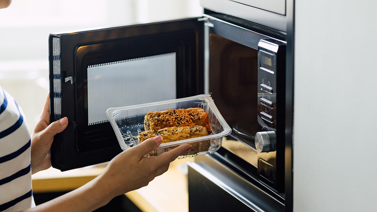 woman reheating a meal in a microwave oven
