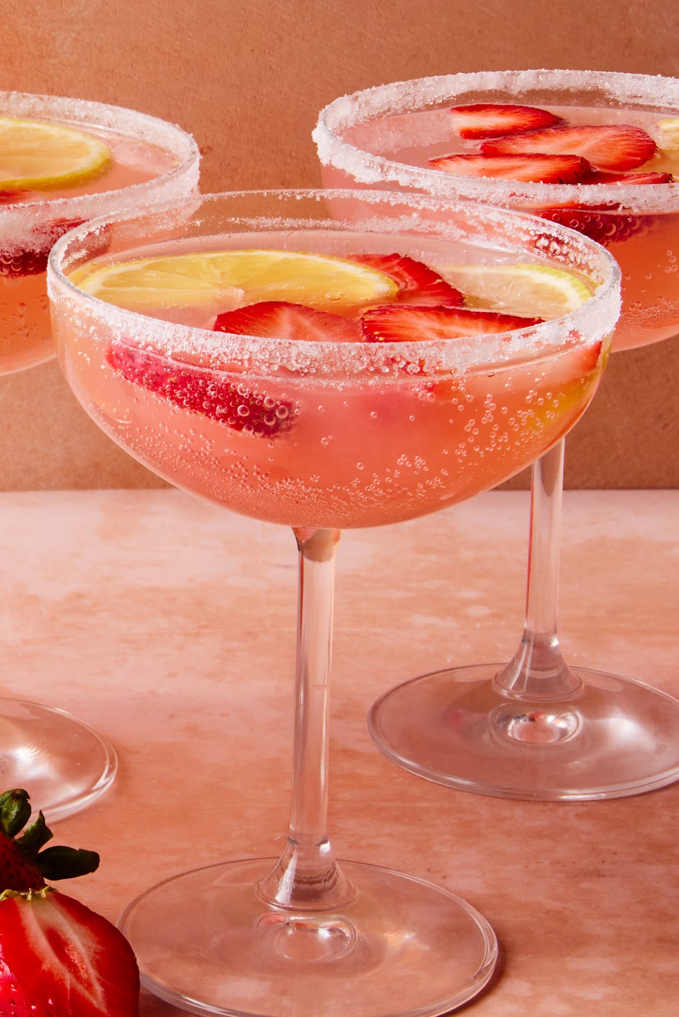 pink cocktail with sliced strawberries and lemon
