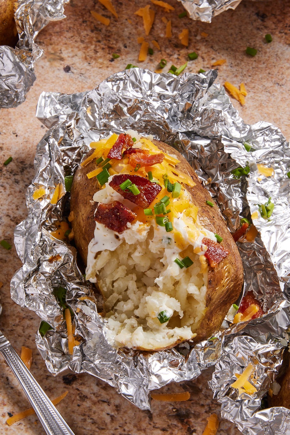 grilled baked potatoes in foil topped with sour cream, bacon, chives, and cheese