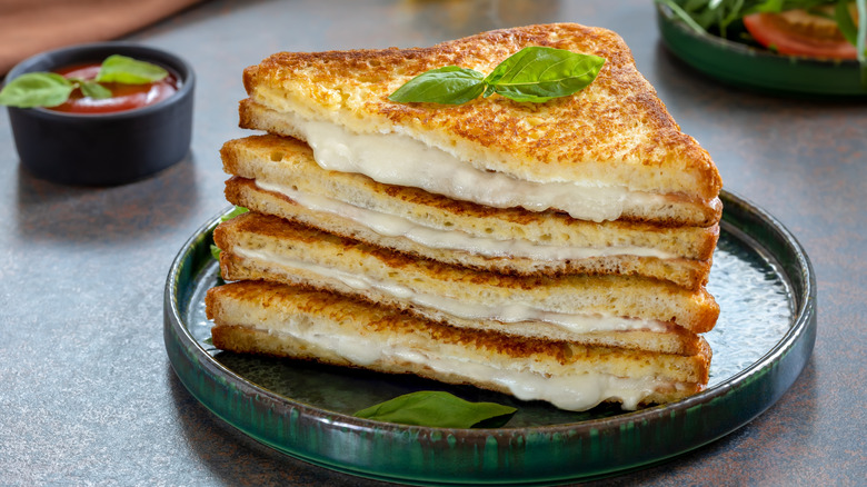 Two grilled sandwiches, diagonally halved and stacked atop eachother, showing melted mozzarella cheese oozing out