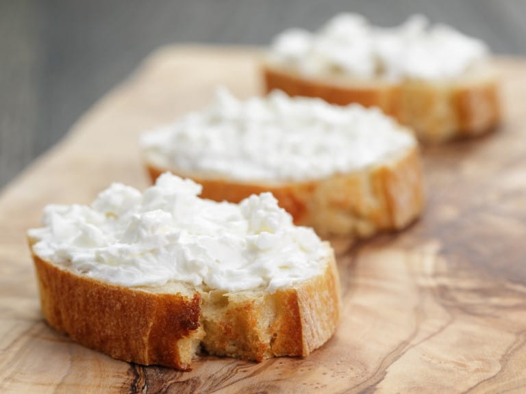 Crunchy baguette slices with cream cheese on an olive board