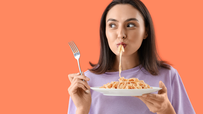 Woman eating pasta with solid peach-colored background