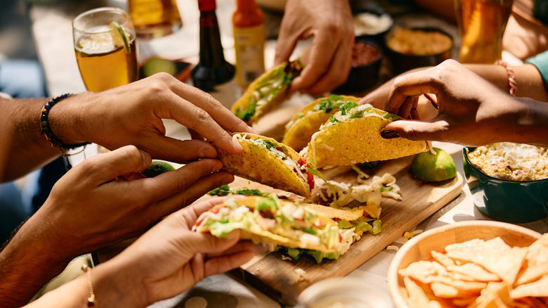 Hands grabbing tacos from a board