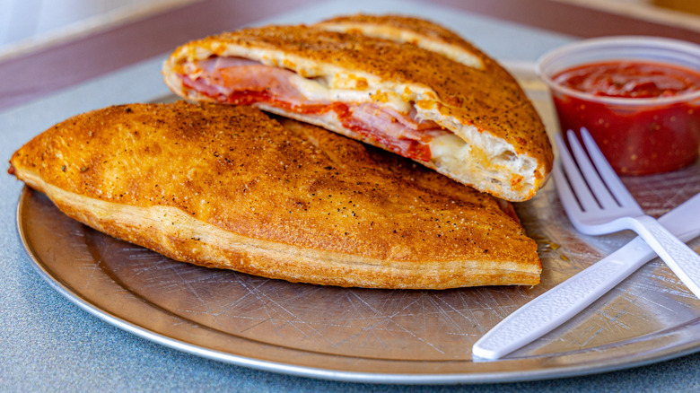 A calzone cut in half on a tray with sauce and plastic utensils