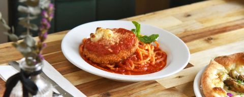 vegan chicken parmesan sits next to a pizza on a wood table